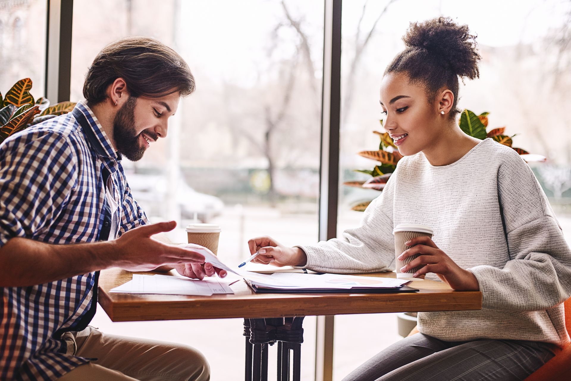 A man and woman at a table, looking at documents and holding coffee cups.