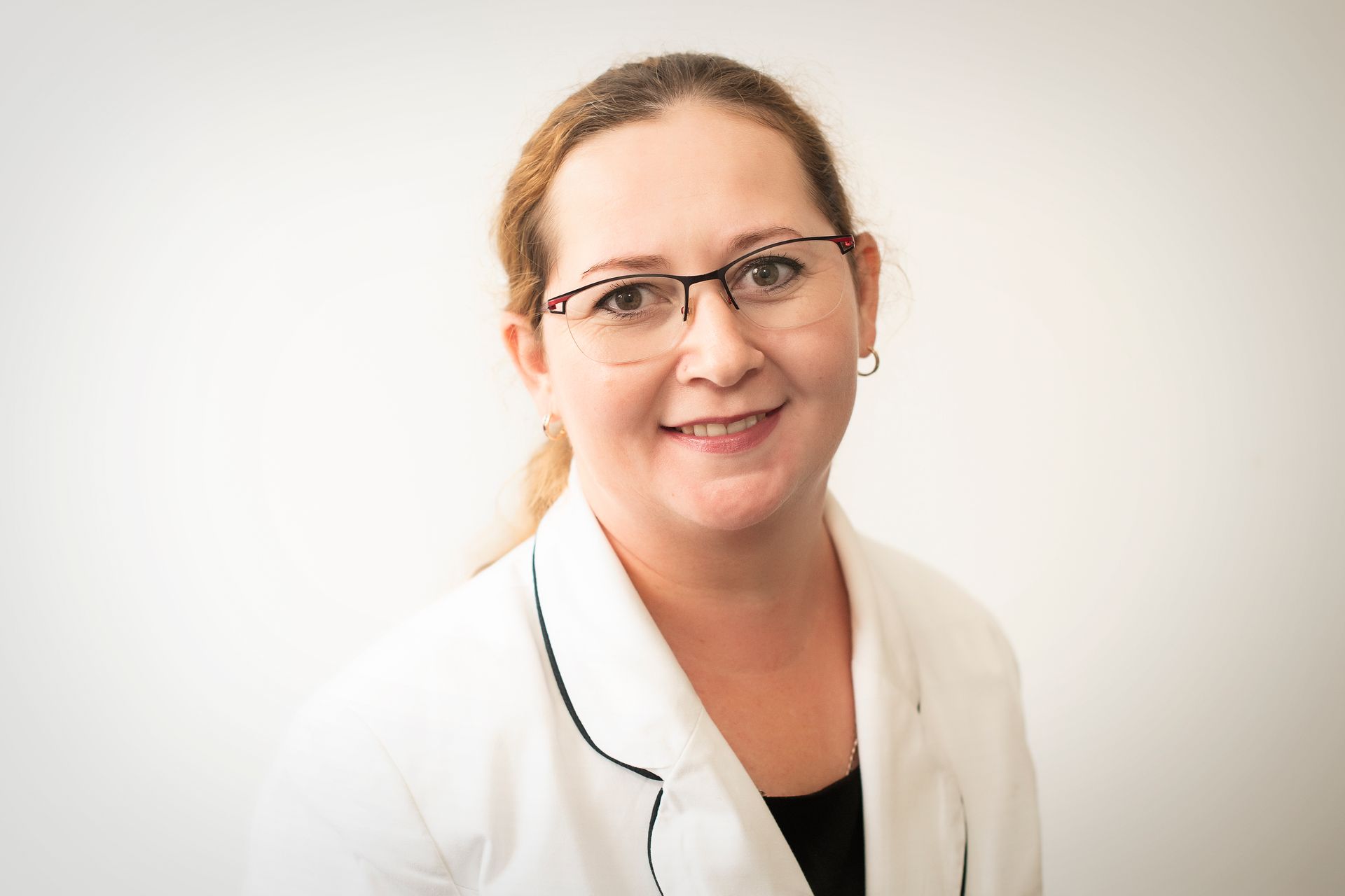 A woman wearing glasses and a white coat is smiling for the camera.
