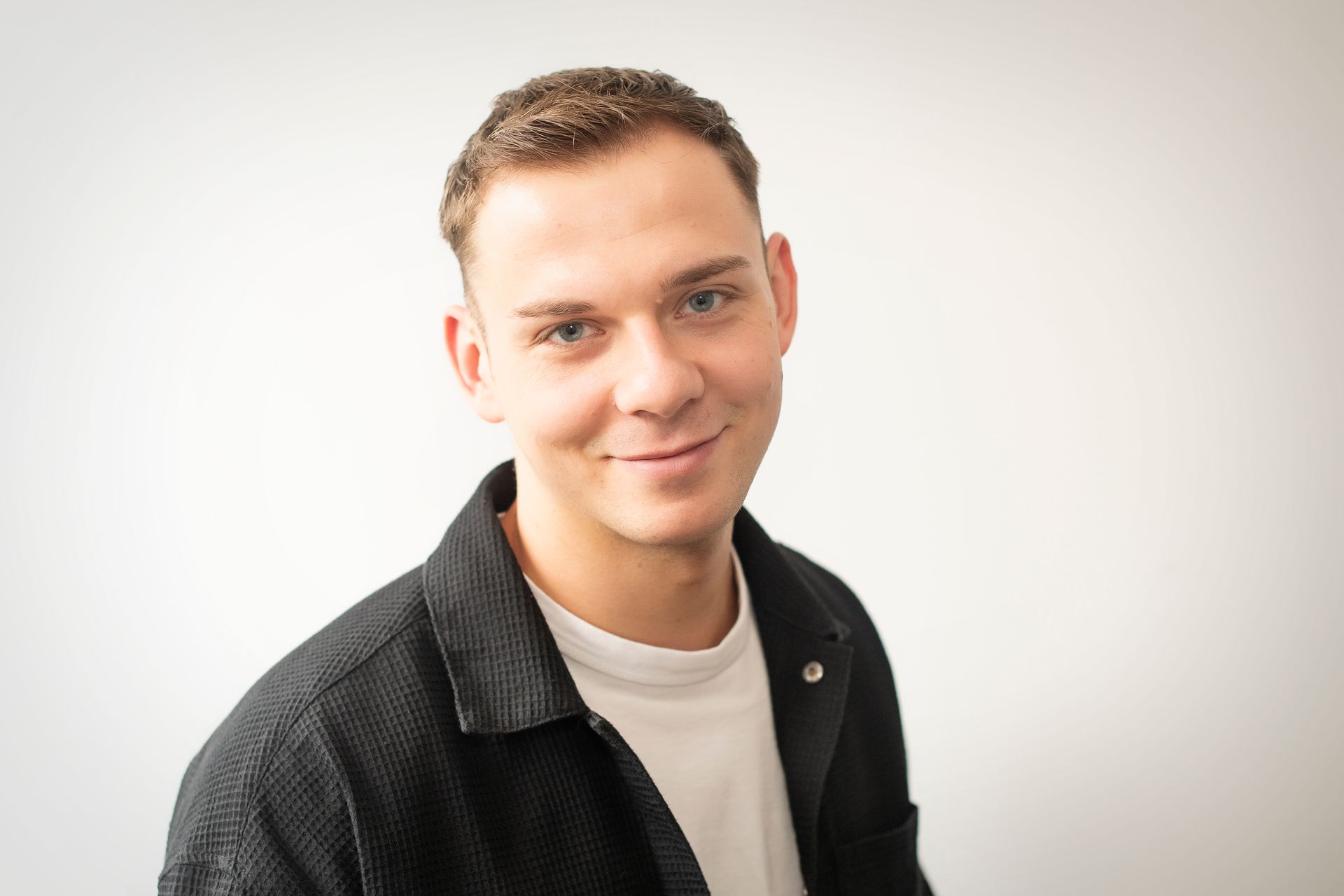 A young man in a black jacket and white shirt is smiling for the camera.