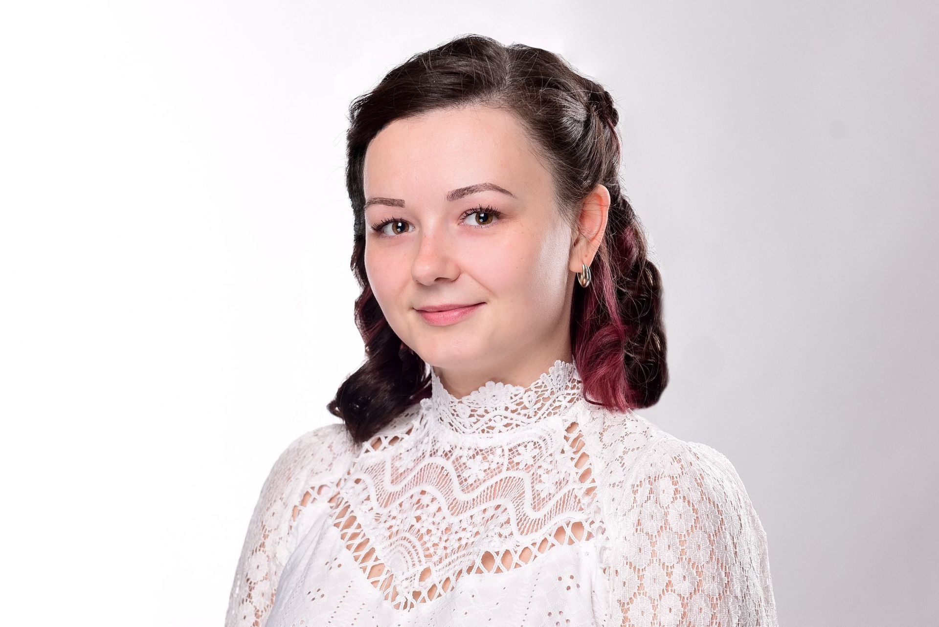 A woman in a white lace top is standing in front of a white background.