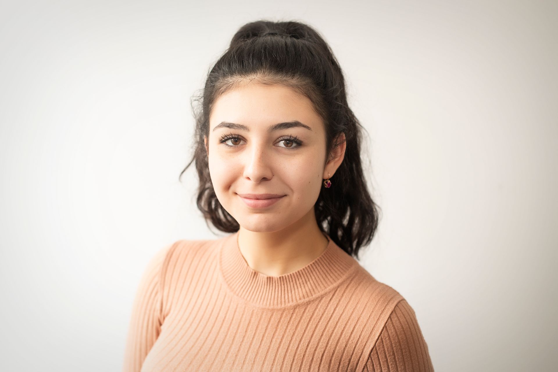 A young woman in a brown sweater is smiling for the camera.