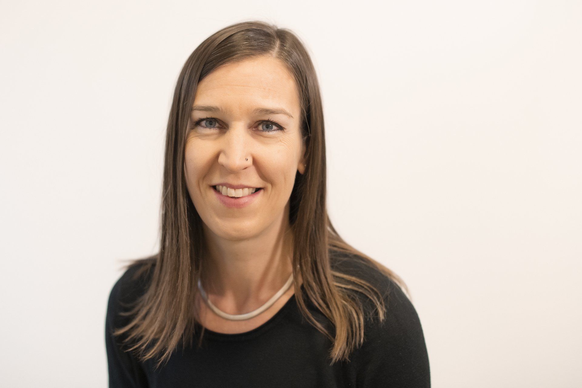 A woman wearing a black shirt and a silver necklace is smiling for the camera.