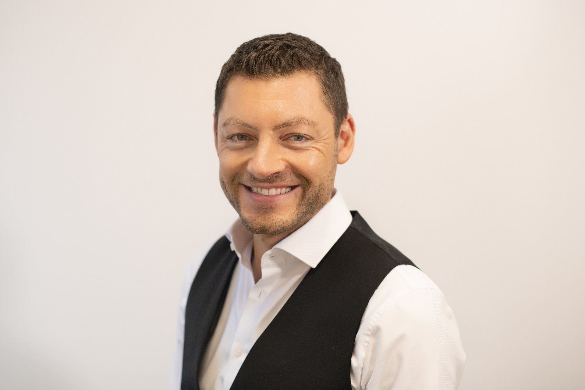 A man in a white shirt and black vest is smiling for the camera.