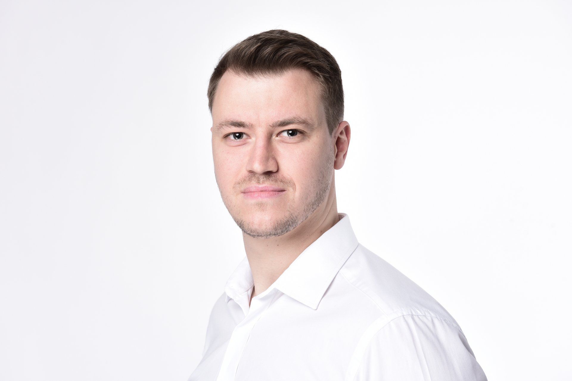 A man in a white shirt is standing in front of a white background.