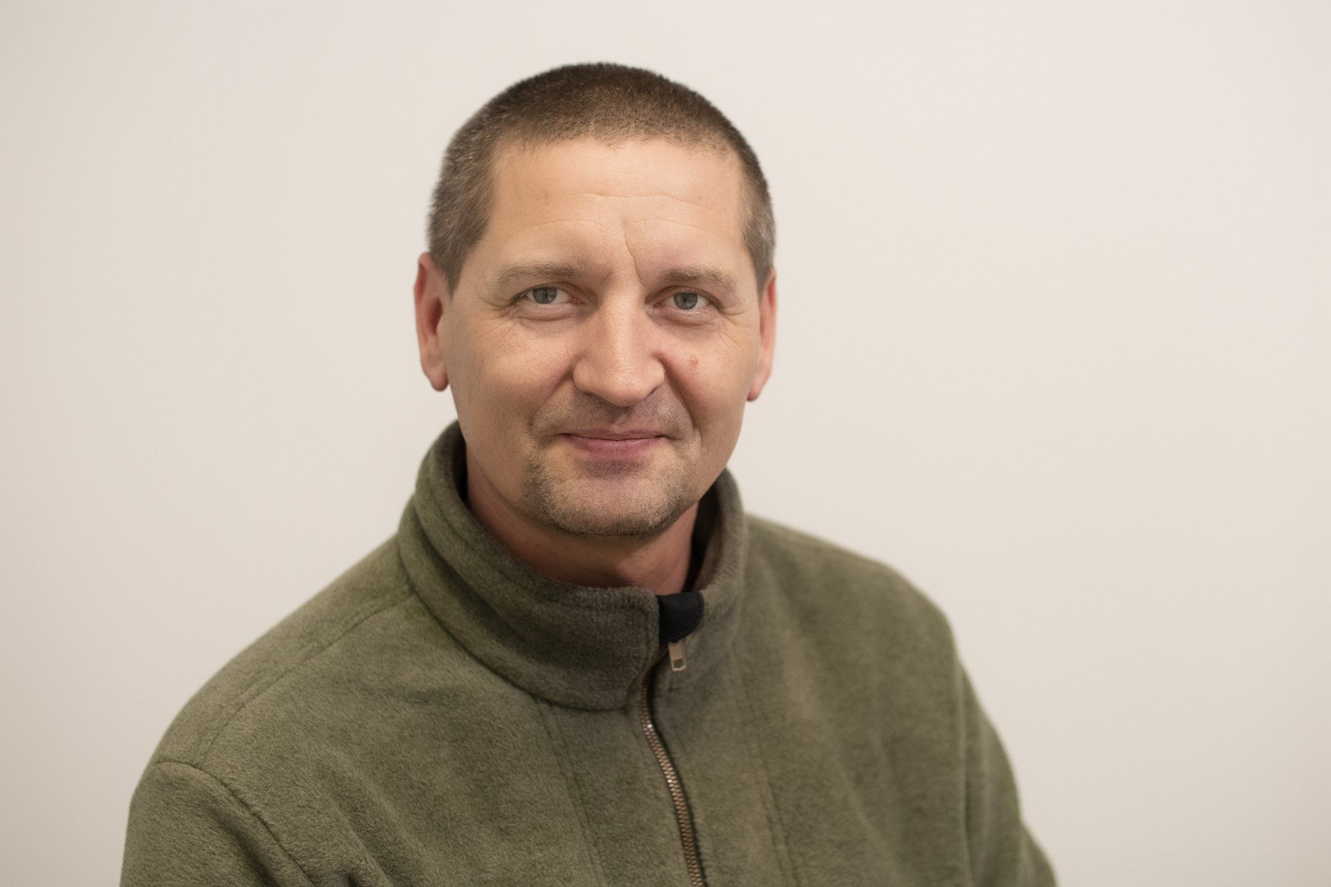 A man in a green sweater is smiling for the camera.