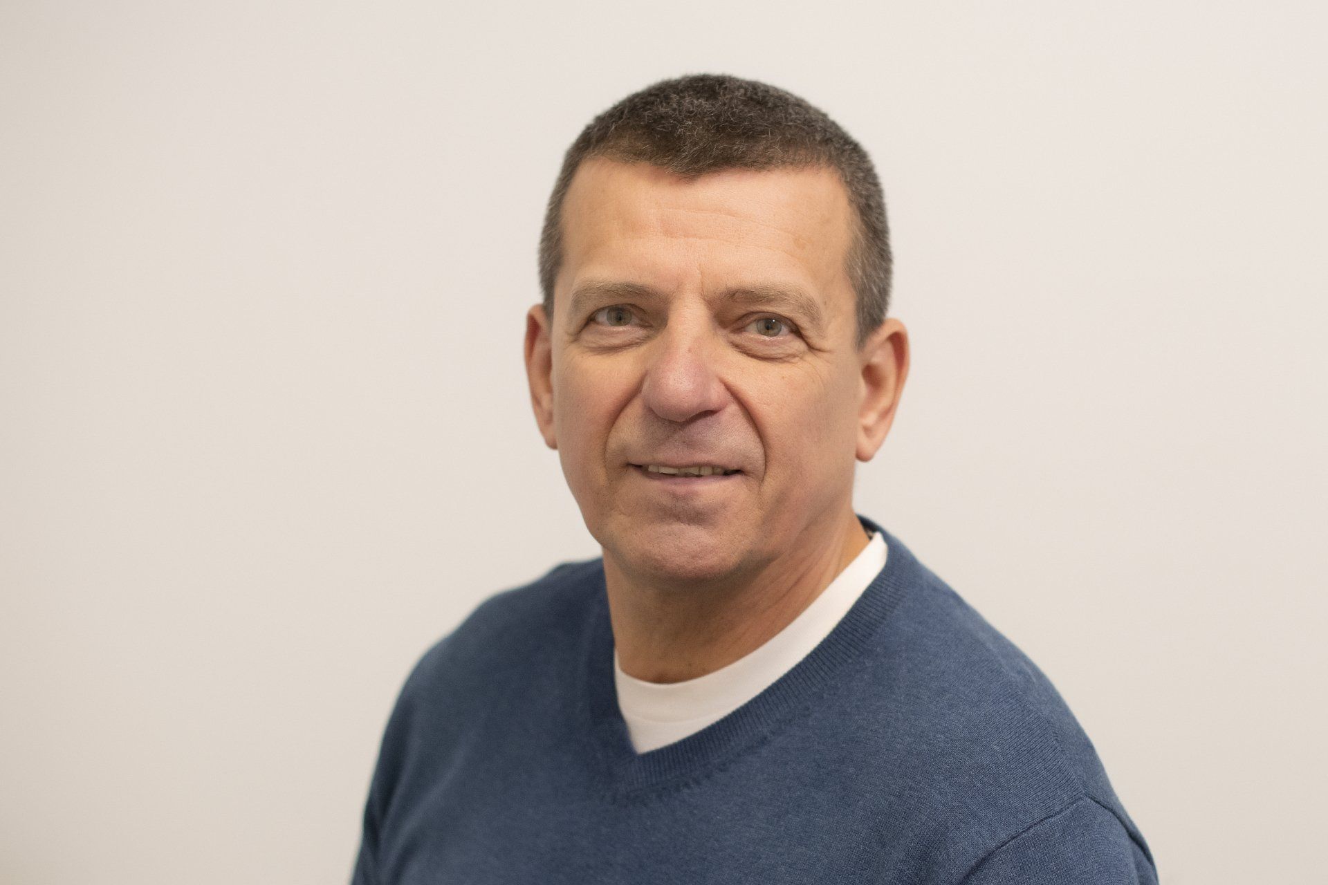 A man wearing a blue sweater and a white shirt is smiling for the camera.