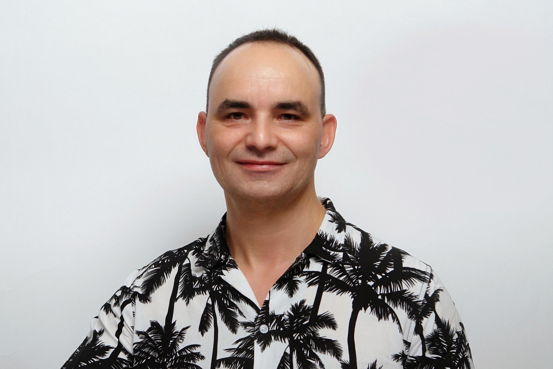 Ein Mann in einem schwarzweißen Hemd mit Palmen darauf lächelt in die Kamera.