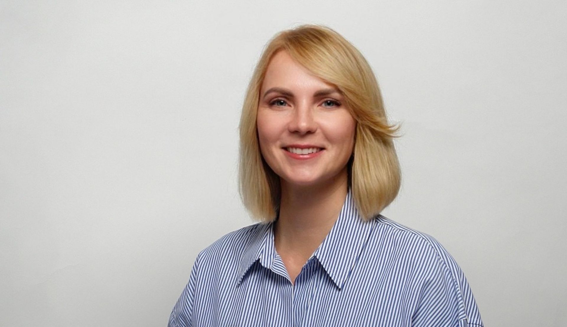 Eine Frau in einem blau-weiß gestreiften Hemd lächelt in die Kamera.
