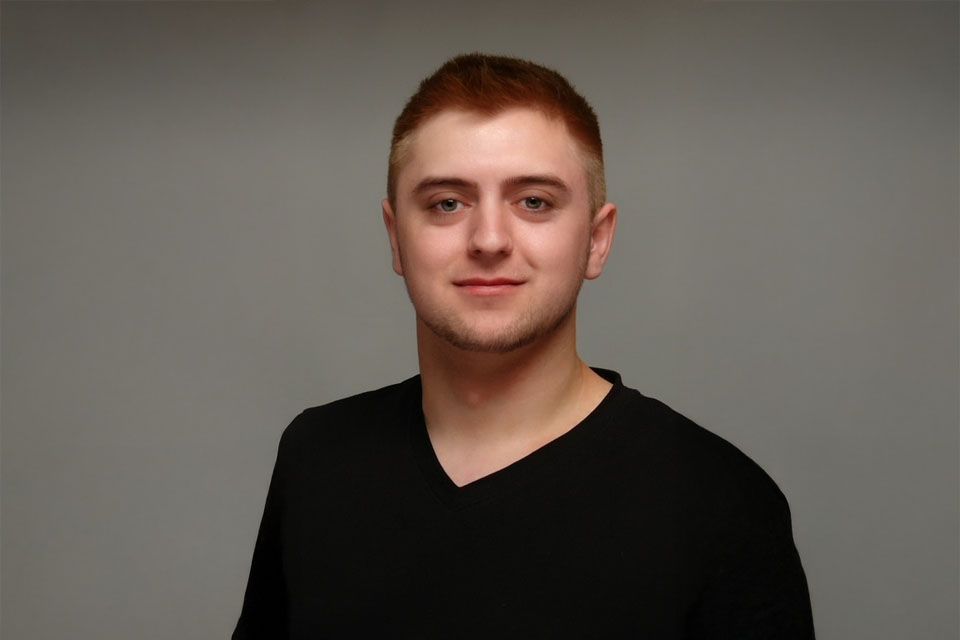 Ein junger Mann in einem schwarzen Hemd lächelt in die Kamera.