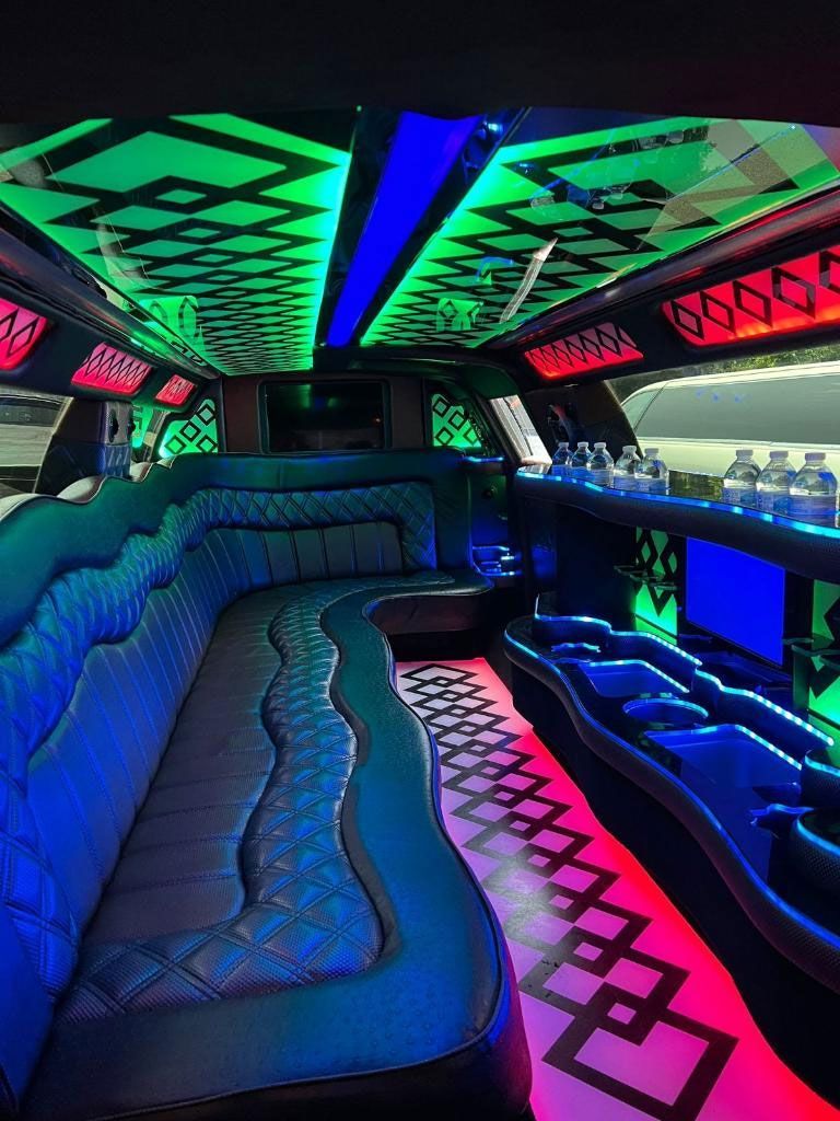Inside of a limousine with blue leather seating, colorful LED lighting, and a bar area.