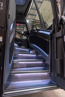 Bus interior with lit steps leading to driver's area, visible door, and dashboard.