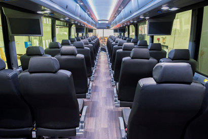 Interior of a bus with rows of black seats, wooden floor, and overhead lighting.