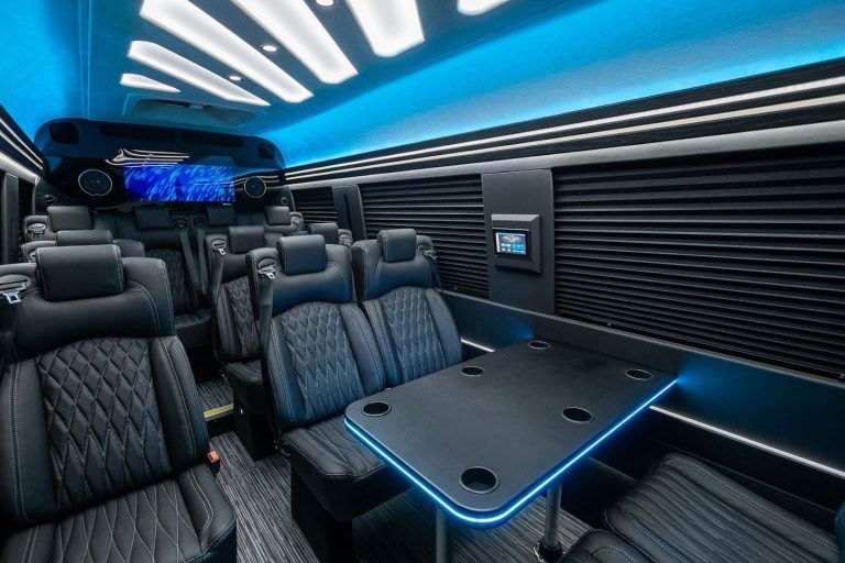 Interior of a luxury van with black leather seating, a table, and blue ambient lighting.