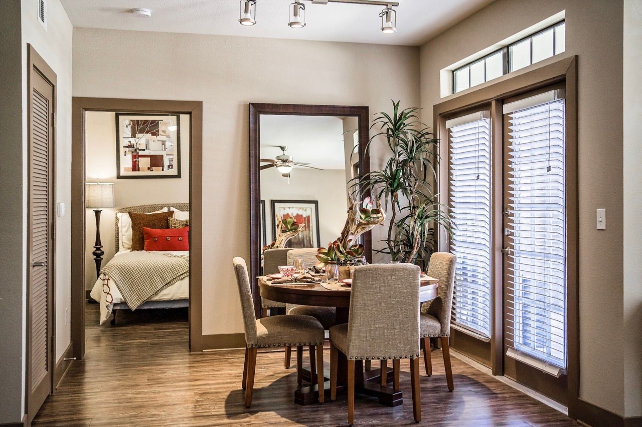Dining area in an apartment with a round table, four upholstered chairs, and large windows with blinds.