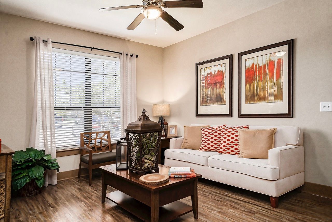 Living room in a modern apartment with a beige sofa, coffee table, and large window with blinds.