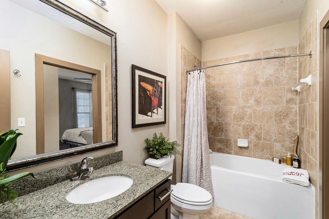 Bathroom with granite vanity, framed mirror, toilet, and tiled tub/shower.