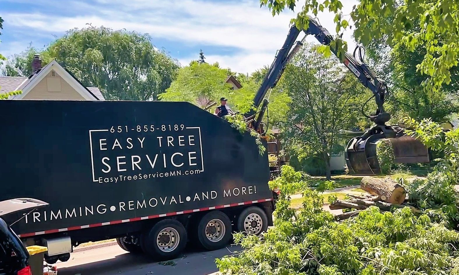 A tree service truck and excavator removing tree branches from a residential area.