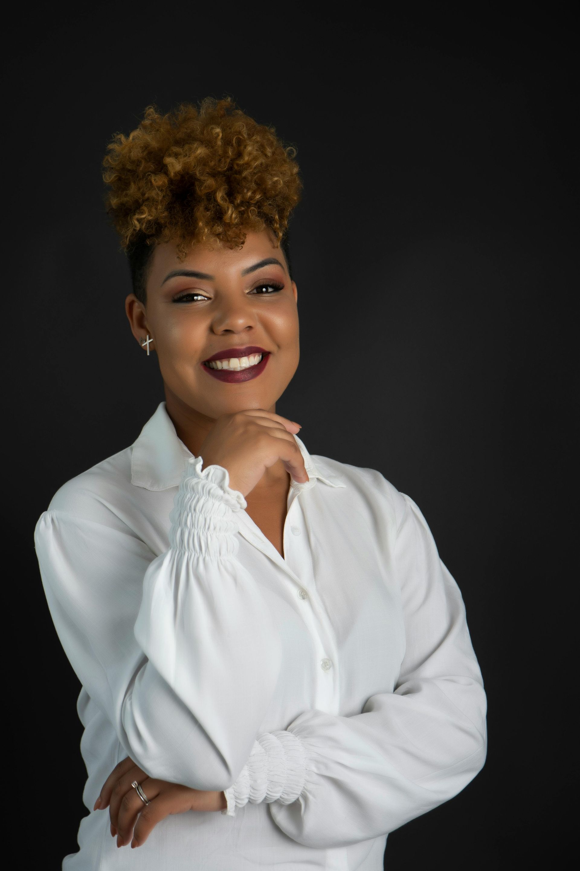 A woman in a white shirt is standing with her arms crossed and smiling. Professional headshot.