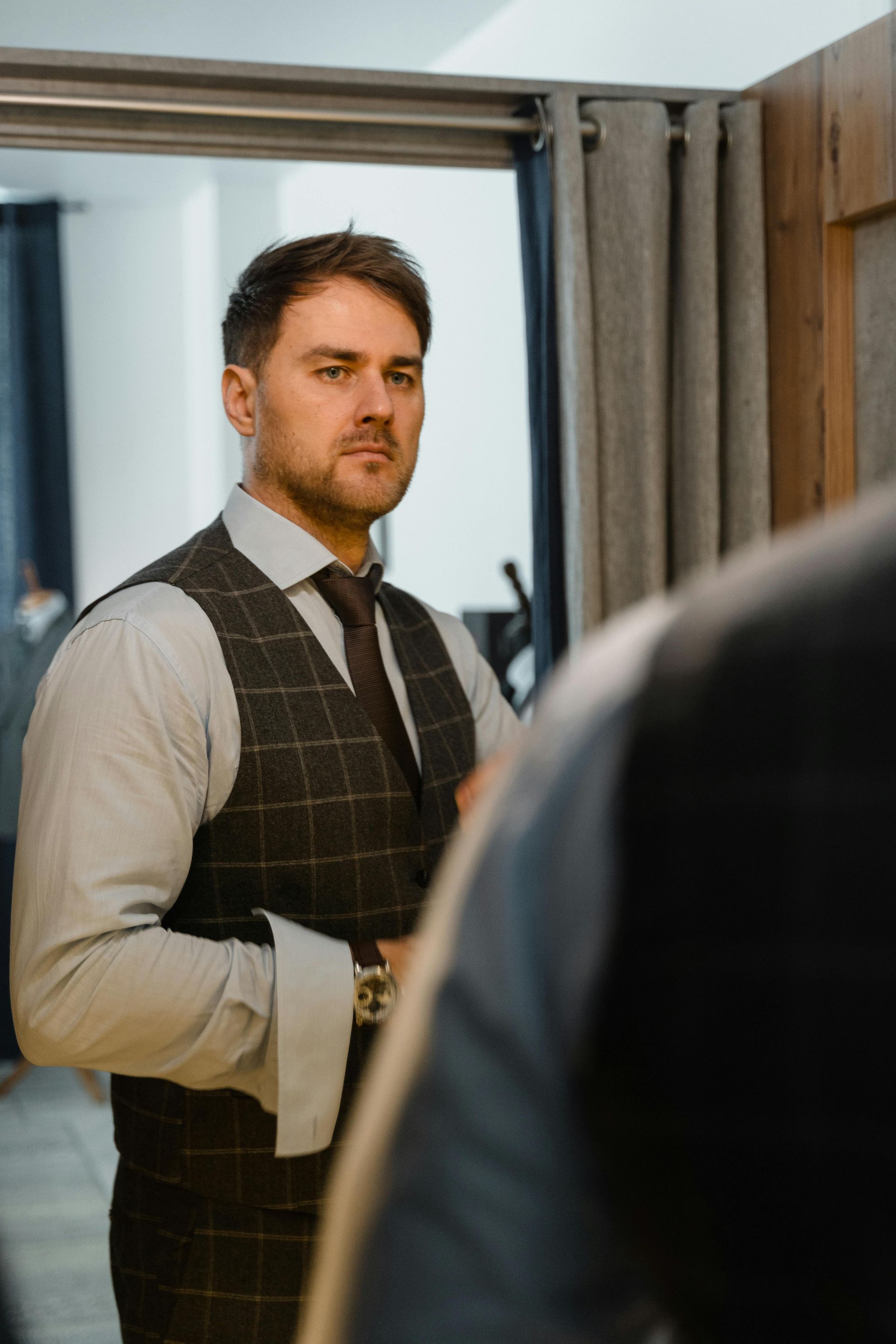 A man in a suit and tie is standing in front of a mirror considering a new professional headshot.