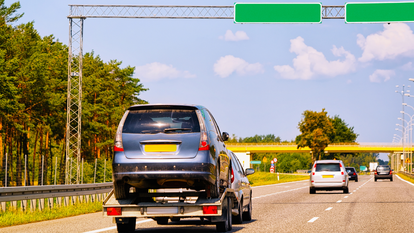 Car being towed on a highway under a green sign. Other cars on the road, sunny day.