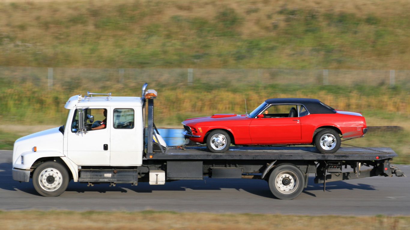 White tow truck carrying a red classic car on a highway.