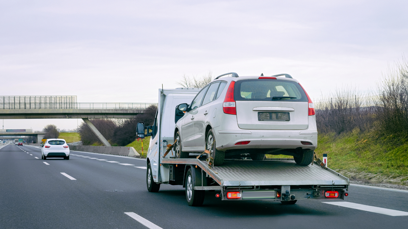 A silver station wagon being towed on a highway by a white tow truck.