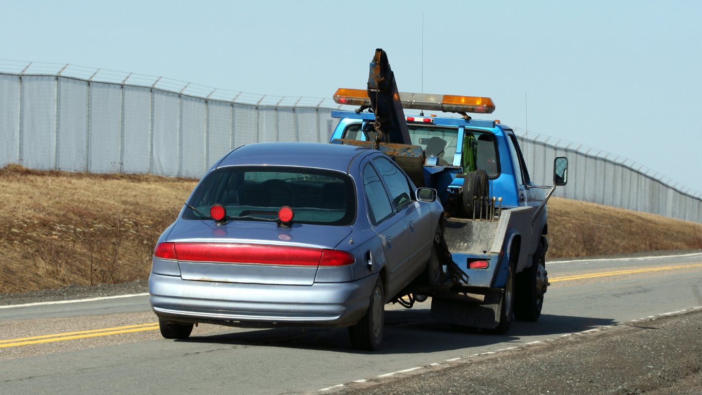 A blue tow truck towing a blue sedan on a highway.