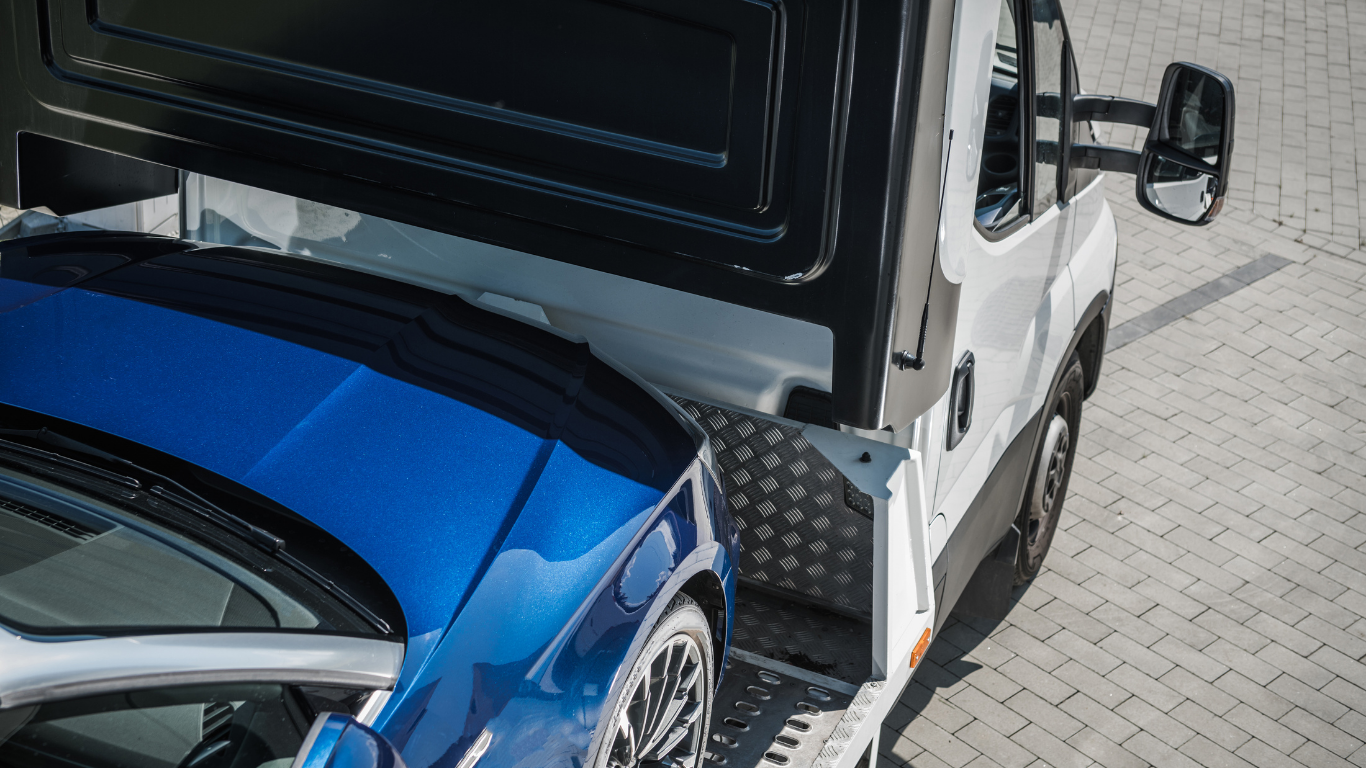 Blue car being loaded onto a white truck on a paved surface.