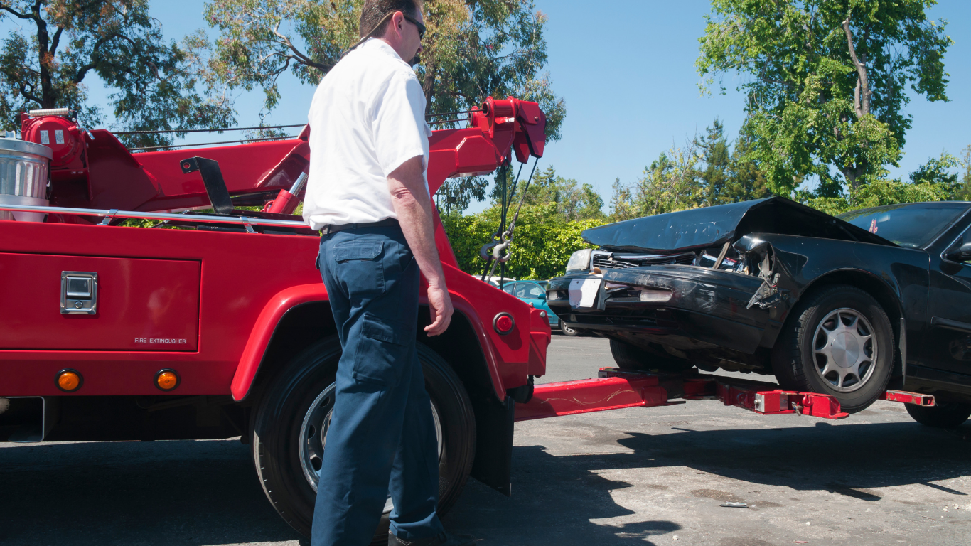 Tow truck operator preparing to tow a black car with front-end damage.