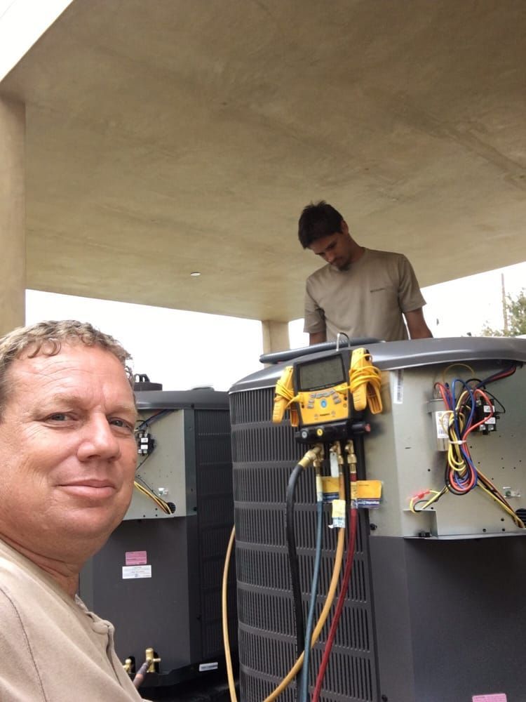 A man is standing in front of an air conditioner while another man works on it