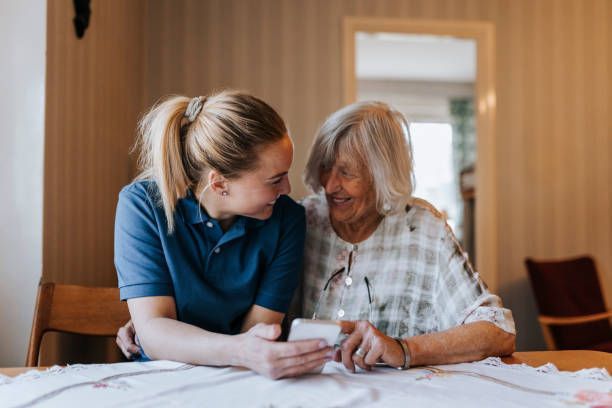 A nurse is helping an elderly woman use a cell phone.