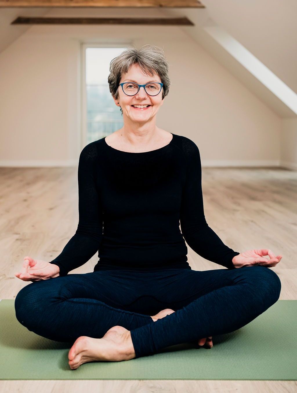 En kvinde sidder i lotusstilling på en yogamåtte.