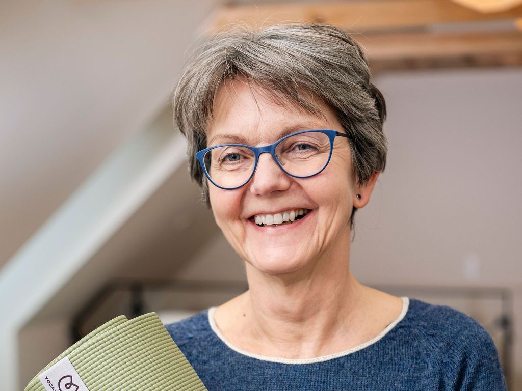 Tina Høppermann, der bærer briller, smiler, mens hun holder en yogamåtte.
