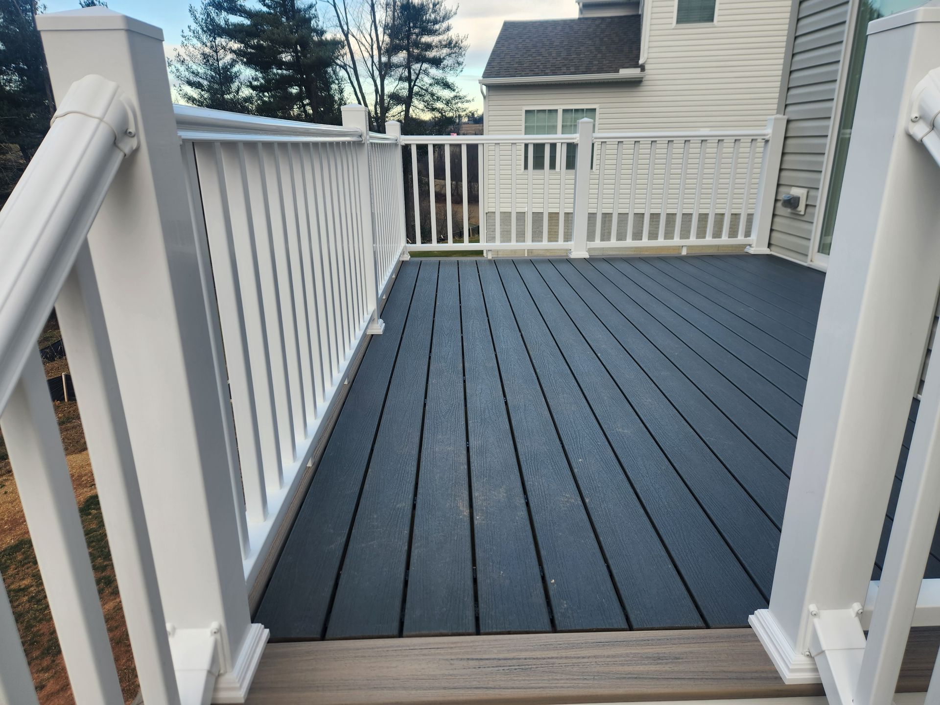 A high-angle view of a dark grey composite deck with white railings attached to the side of a light-colored house.