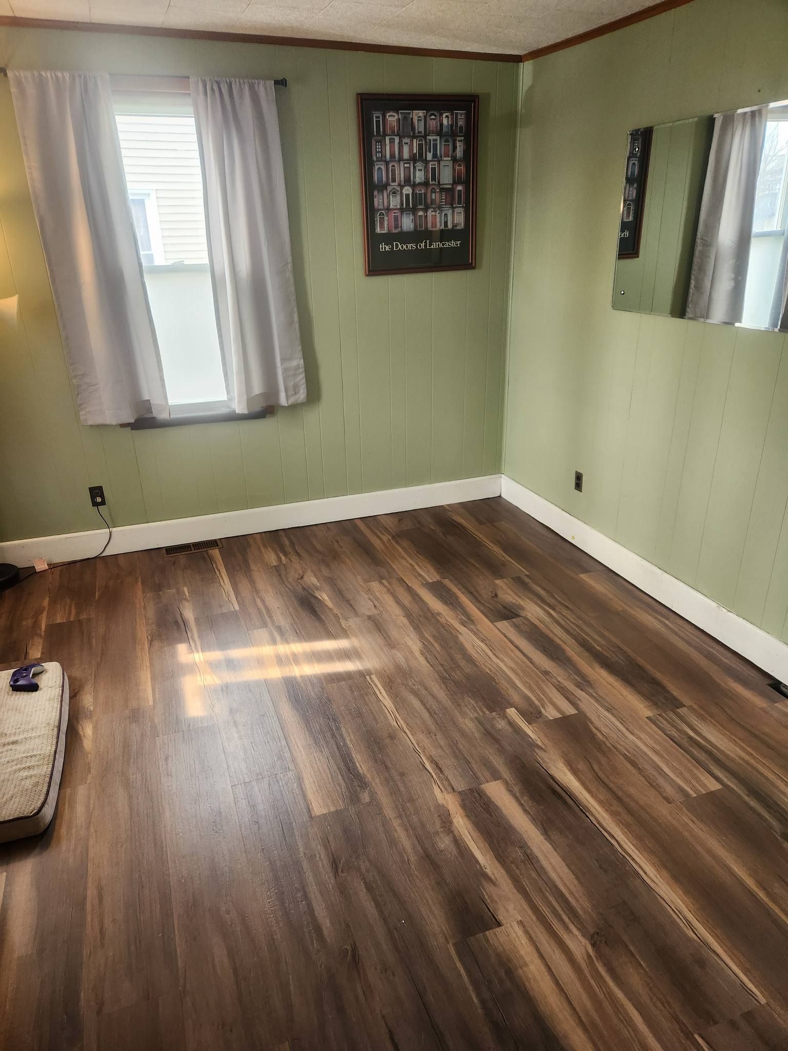 Empty room with wood-look flooring, light green walls, a window with curtains, and a framed picture.