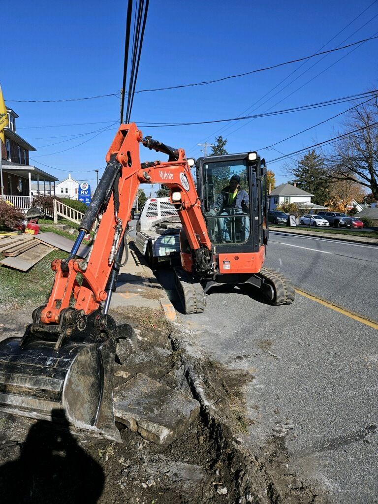 Orange excavator digging along a road, under power lines. Sunlight.