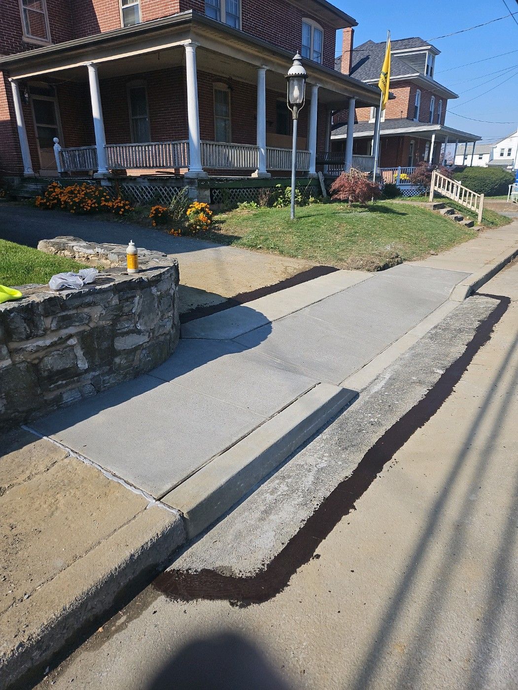 Sidewalk with concrete ramp leading to a building's porch, next to a stone wall and street.