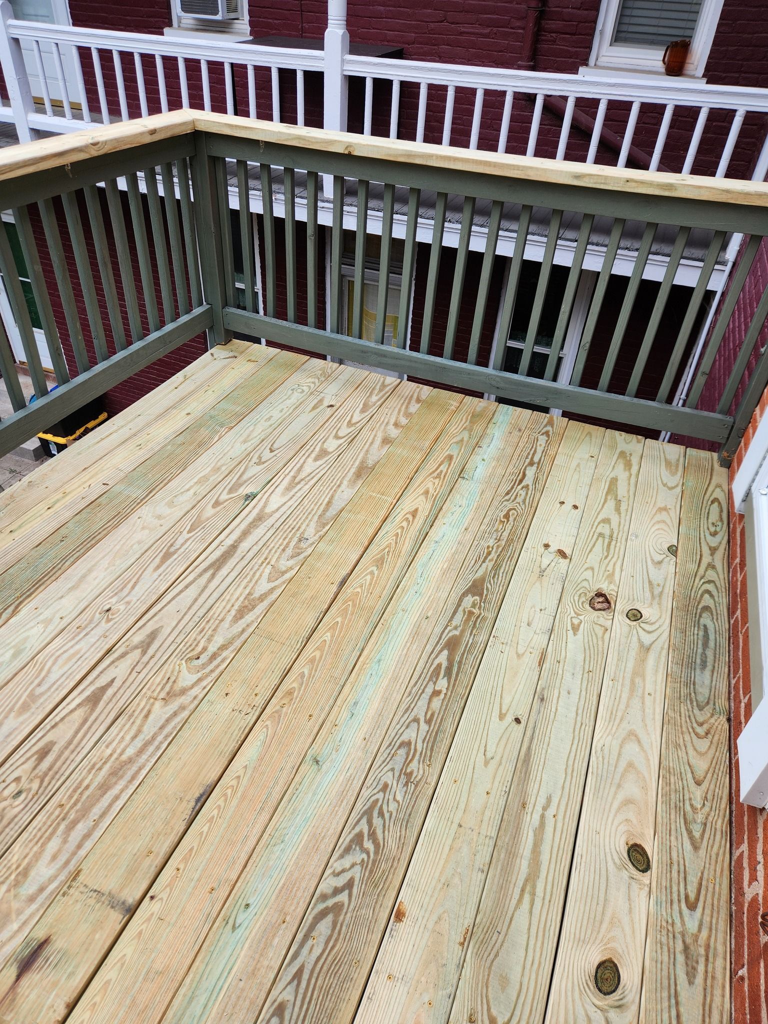 Wooden deck with green railing, overlooking a basement entrance.