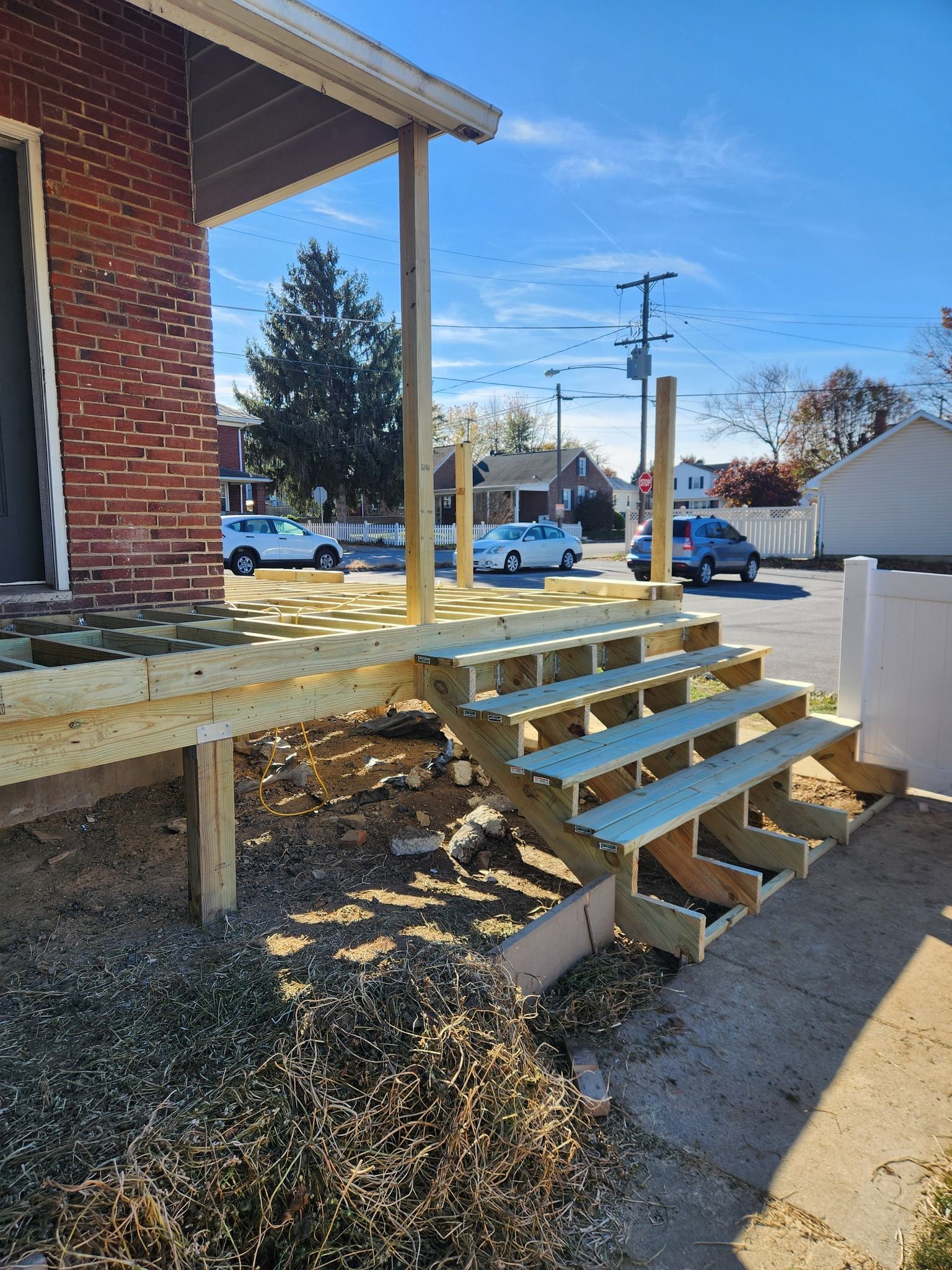 New wooden porch and steps attached to a brick building, under a blue sky, with cars and trees in the background.