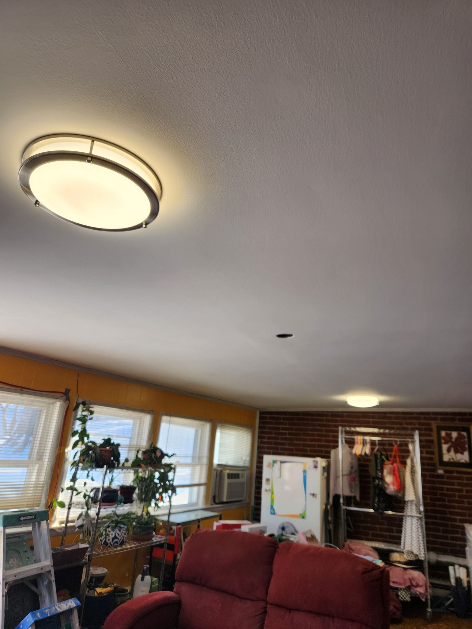 A brightly lit living room with a recliner, windows, a ceiling light, and brick wall.