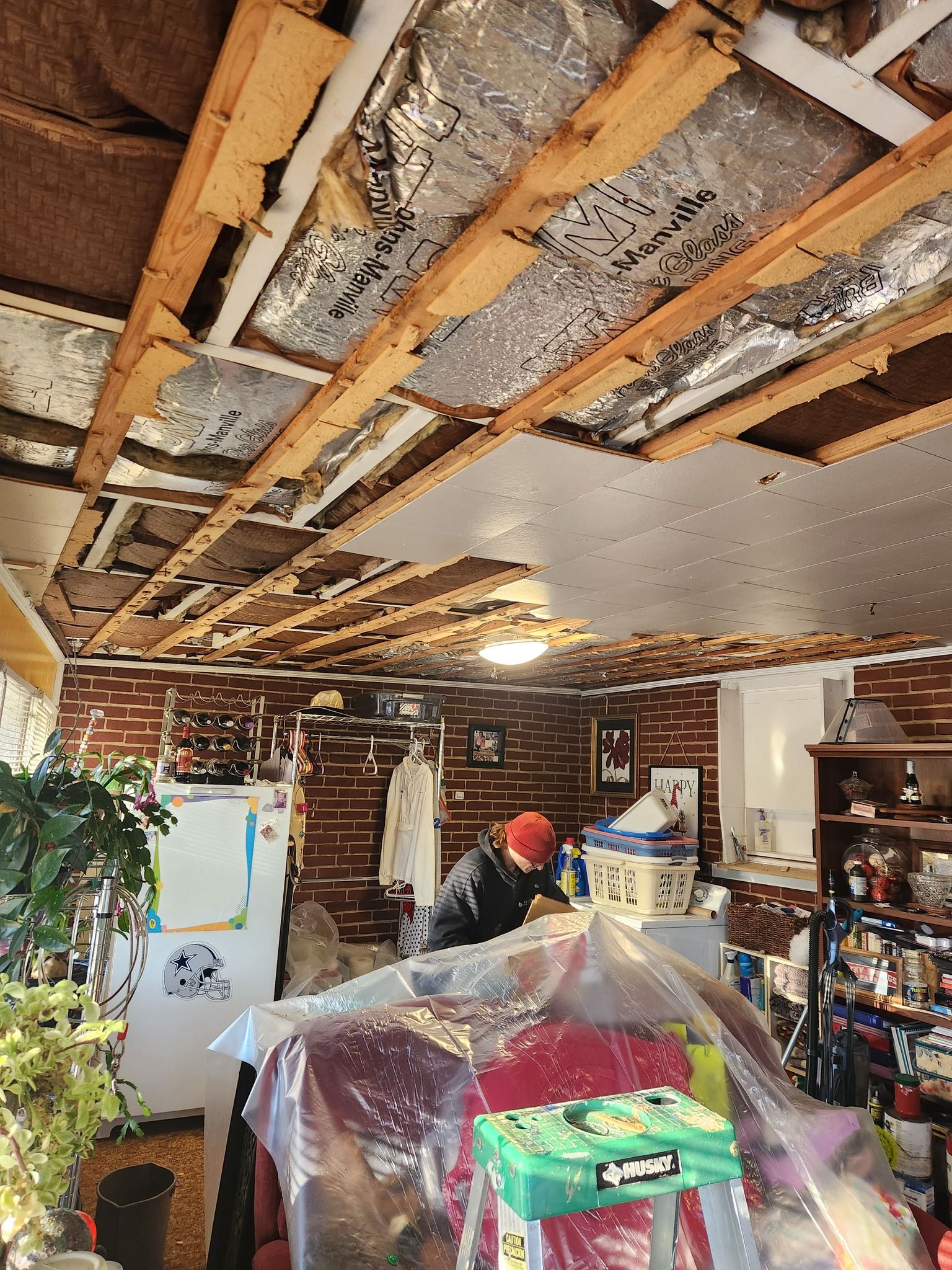 Man working on a damaged ceiling in a room with exposed beams and brick walls.