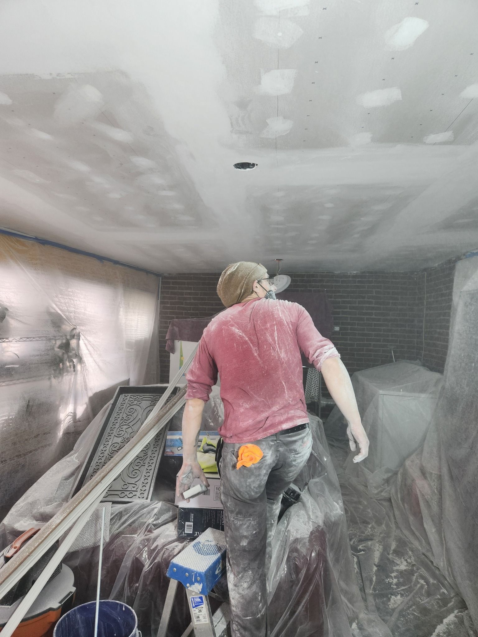 Person in construction zone, covered in dust, working on ceiling.
