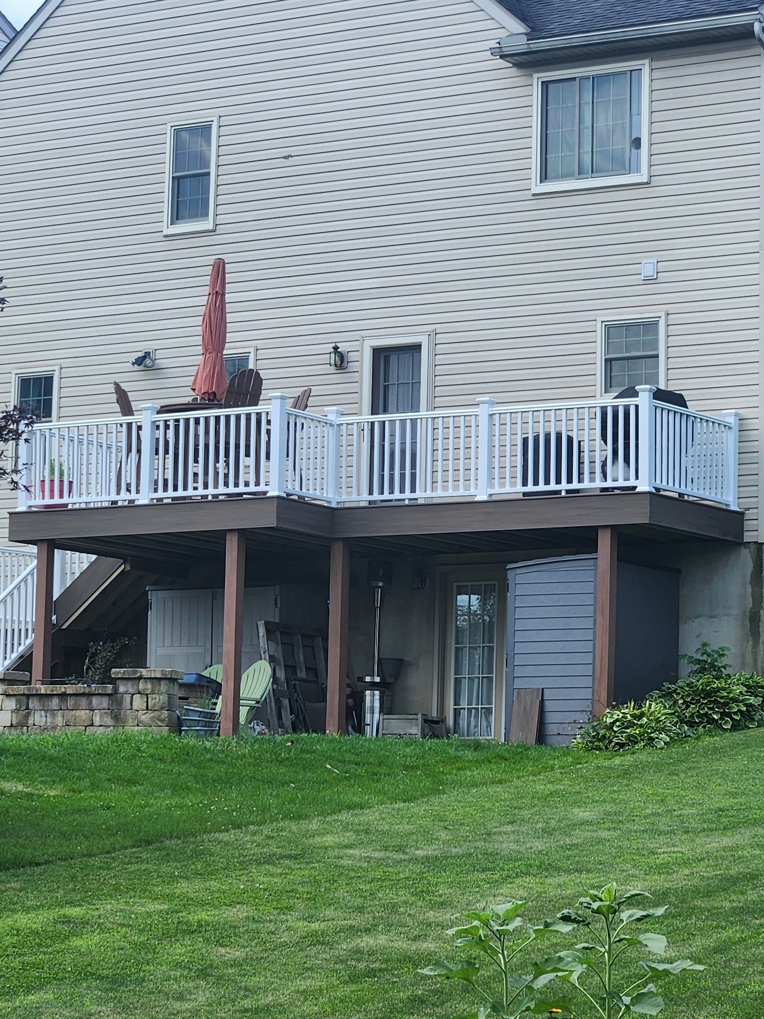 Backyard view of a two-level deck with white railings, a tan house, and a grassy lawn.