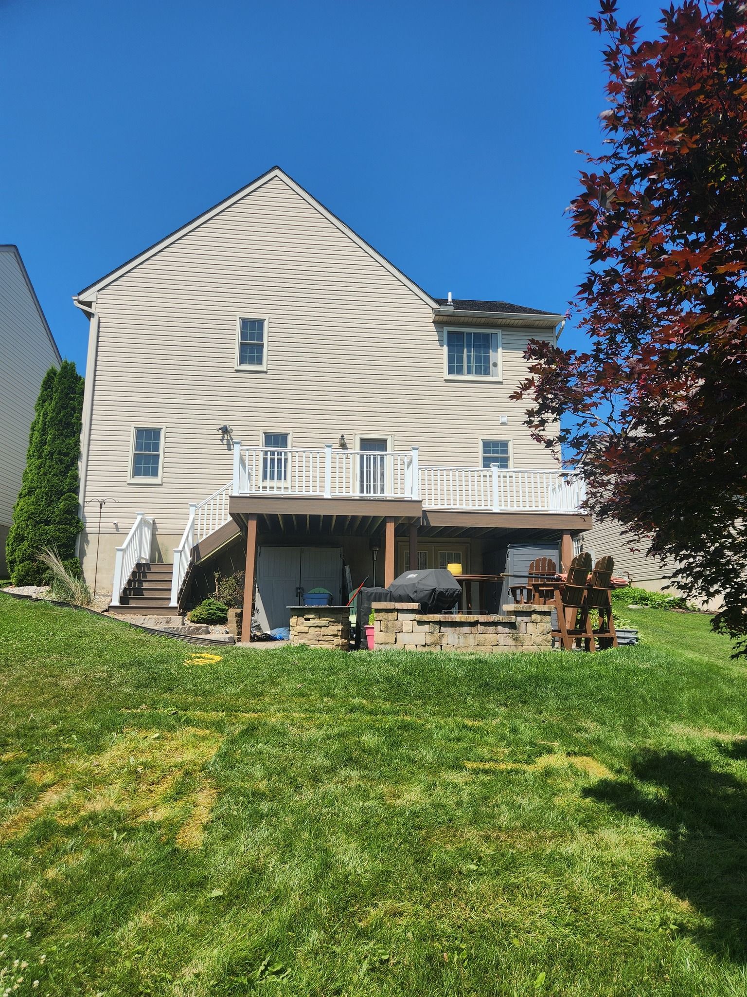 Back view of a two-story beige house with a wooden deck and a brick patio, against a blue sky.