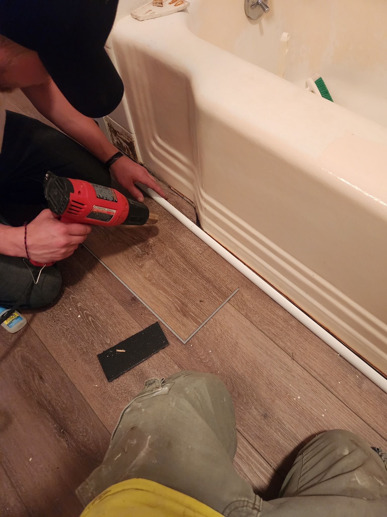Person using a heat gun to apply sealant along a bathtub base on a tiled floor.