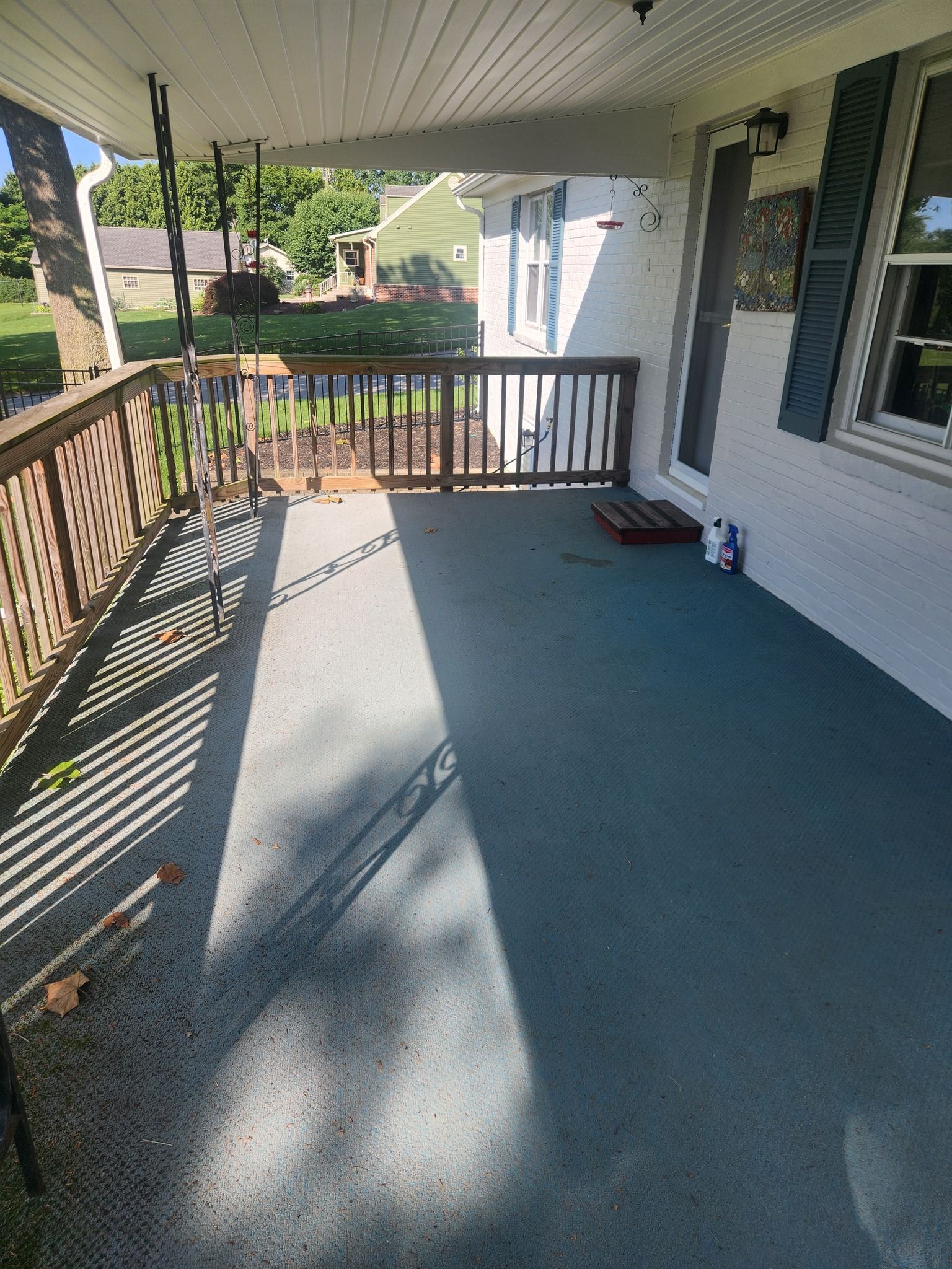 Covered front porch with wooden railing, teal floor, and white brick house.