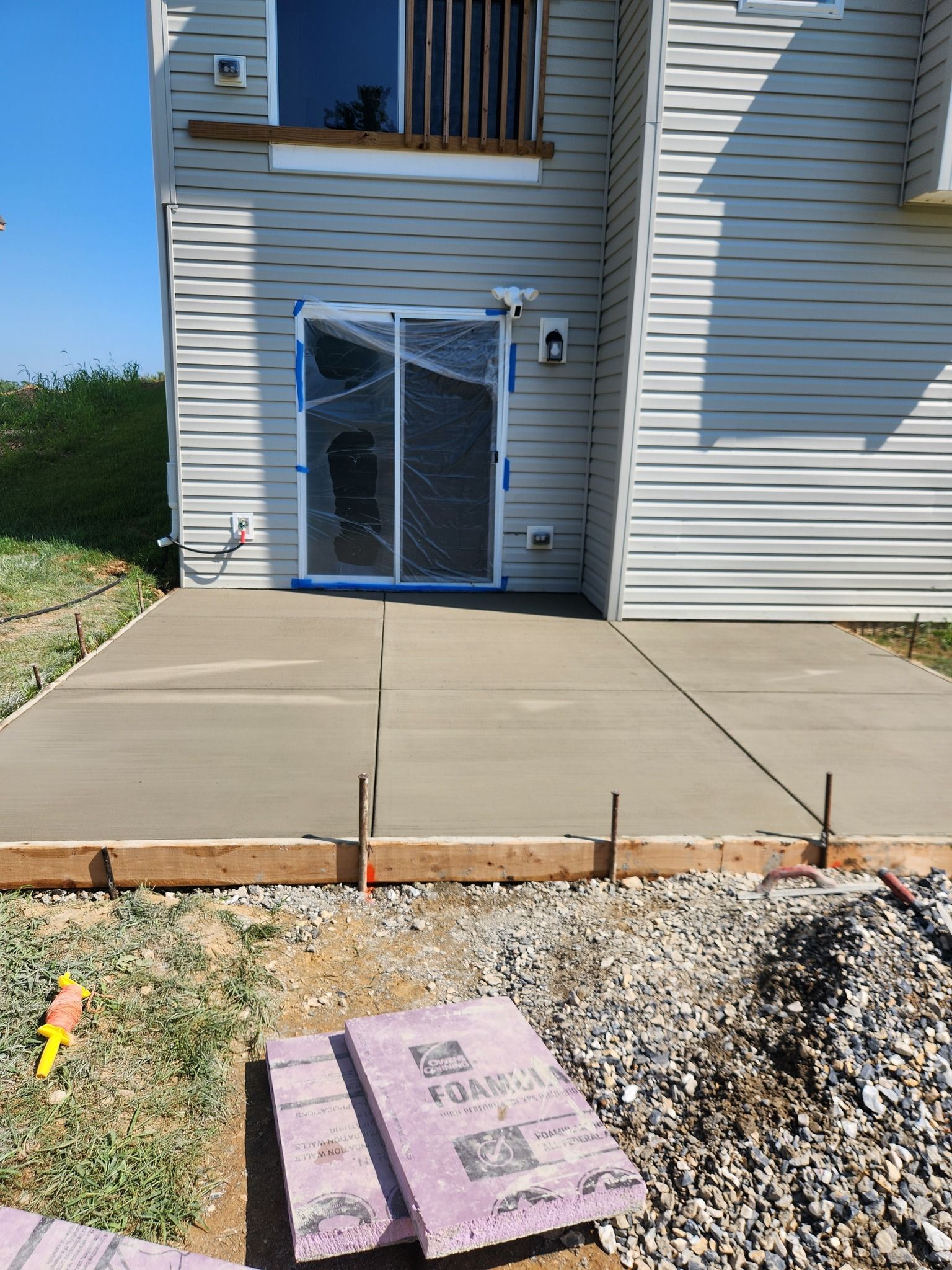 Newly poured concrete patio outside a light gray house with a broken sliding glass door.