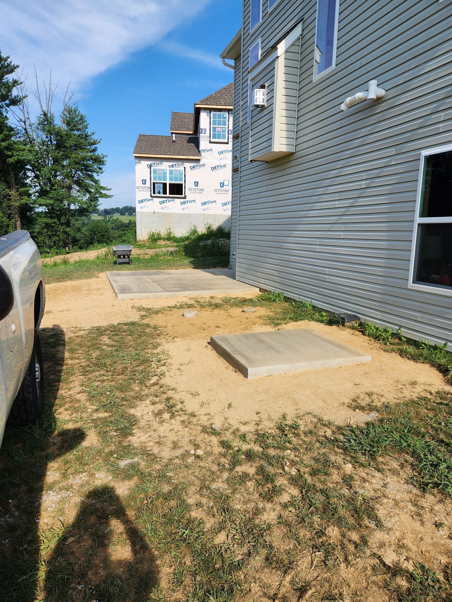Two concrete slabs on dirt, near a building under construction. Sunny day.
