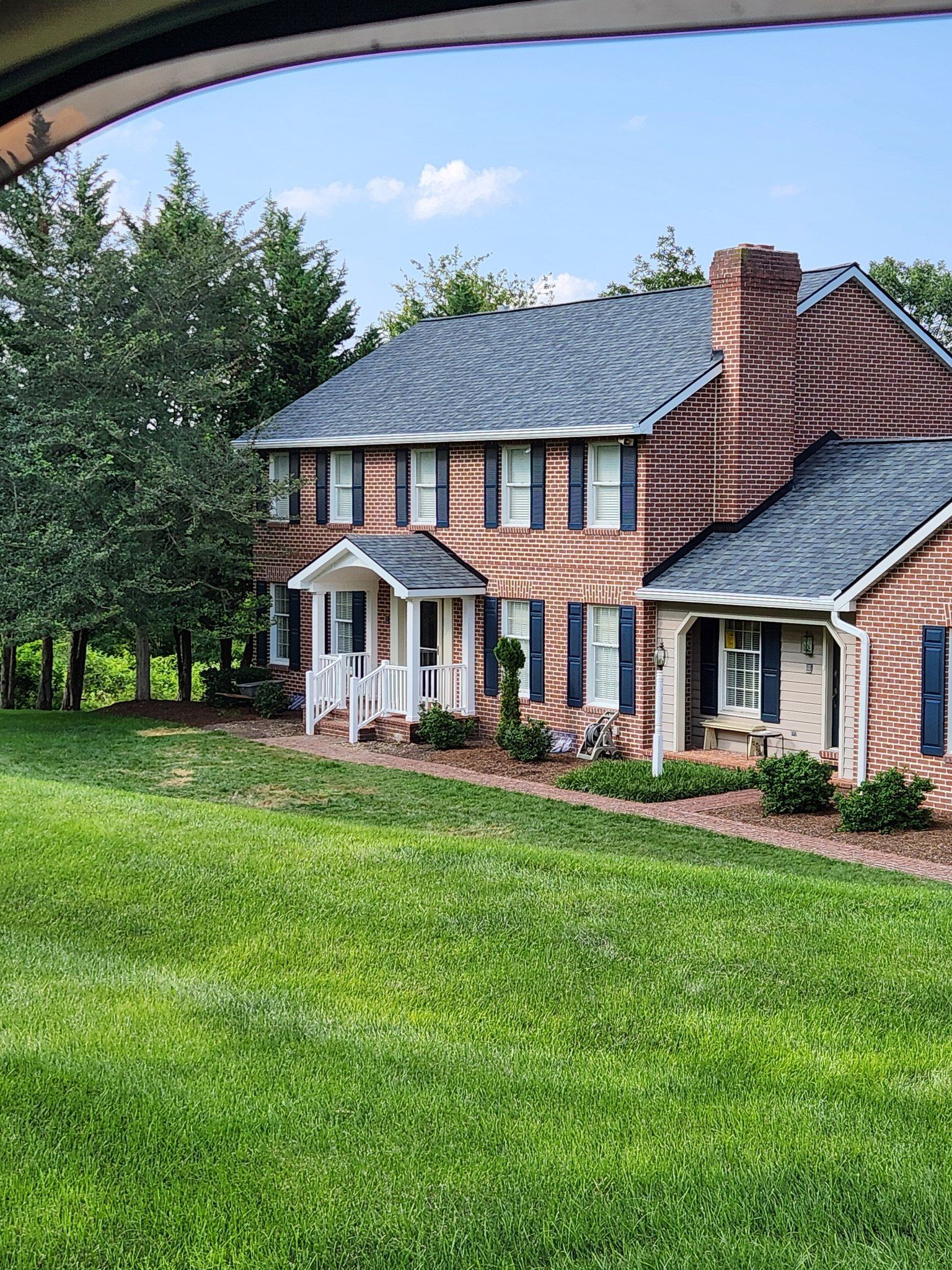 Two-story brick house with black shutters and roof, a porch, and a lush green lawn.