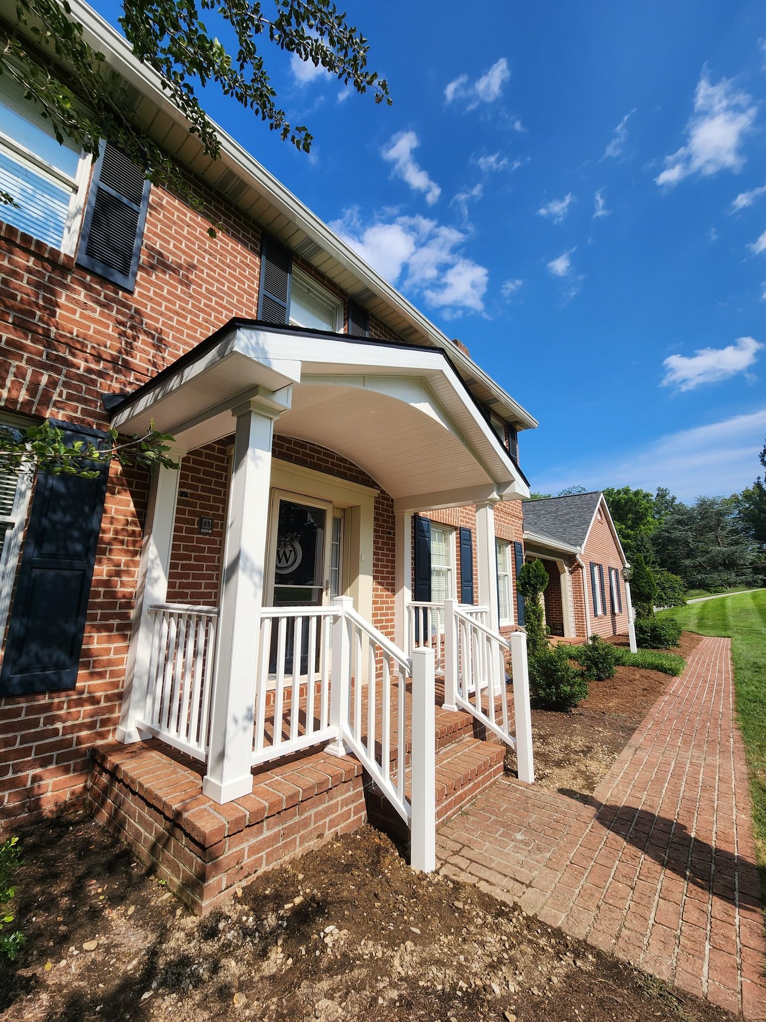 Brick home with white porch and railing, bright blue sky.